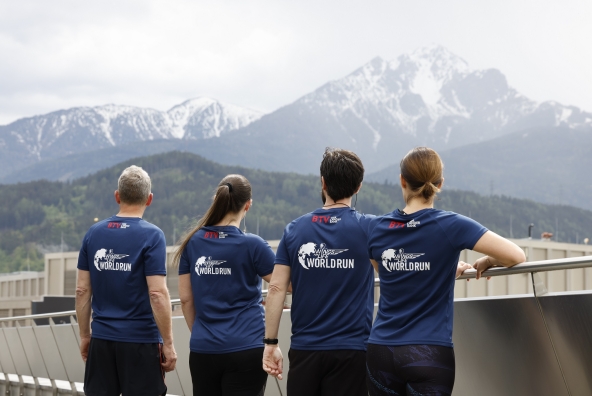 Mitarbeiterinnen und Mitarbeiter mit Wings for Life T-Shirt von hinten fotografiert. Blick auf die Berge.