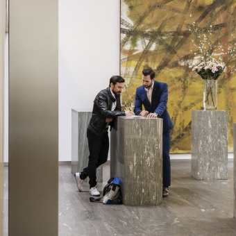 Zwei Männer stehen an einem Stehtisch. Ein Mann unterschreibt ein Dokument.