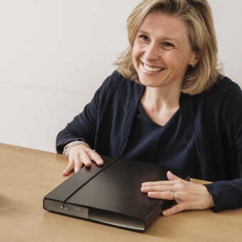 Eine Frau lächelt eine andere Frau an. Sie hat eine schwarze Mappe vor sich liegen.