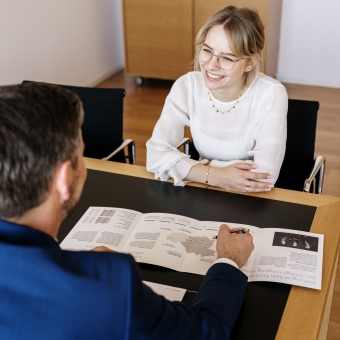 Eine Frau mit Brille schaut einem Mann im blauen Anzug lächelnd an.